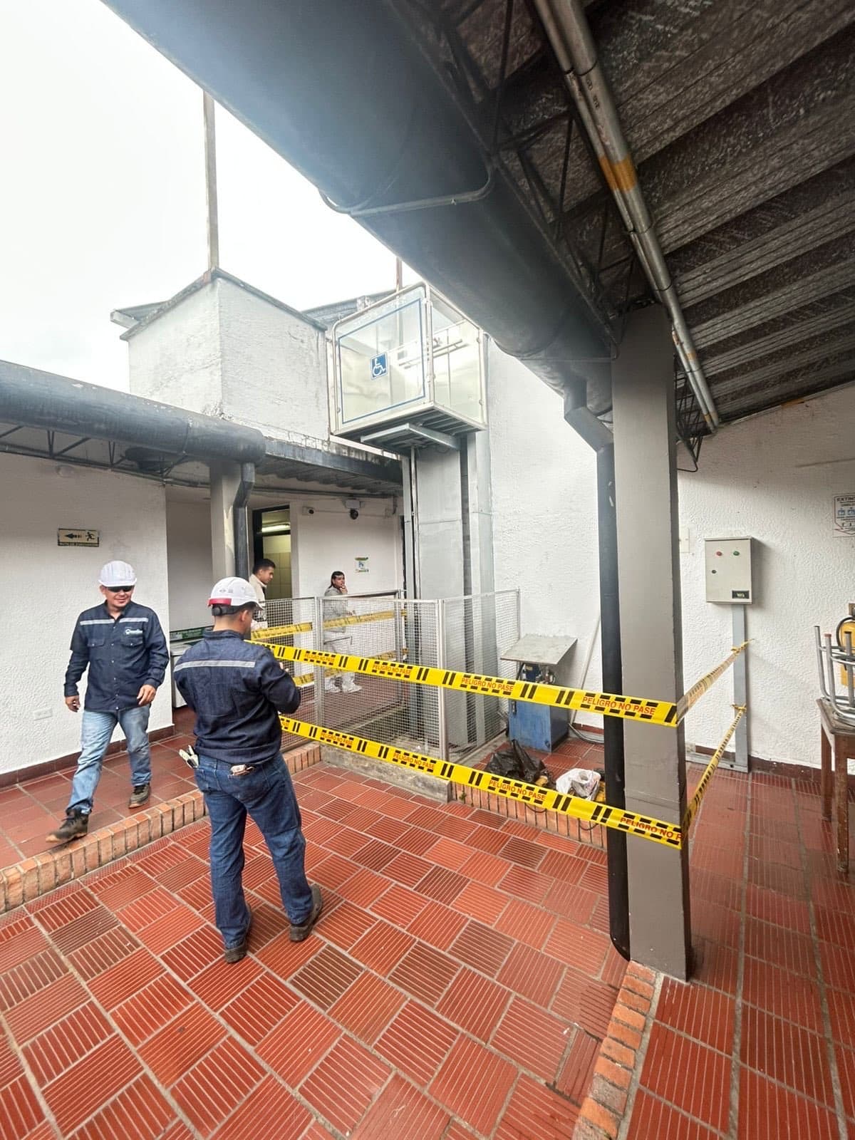 Técnicos de Quantium con casco frente al elevador hidráulico con cabina panorámica instalado en la sede de Ocaña